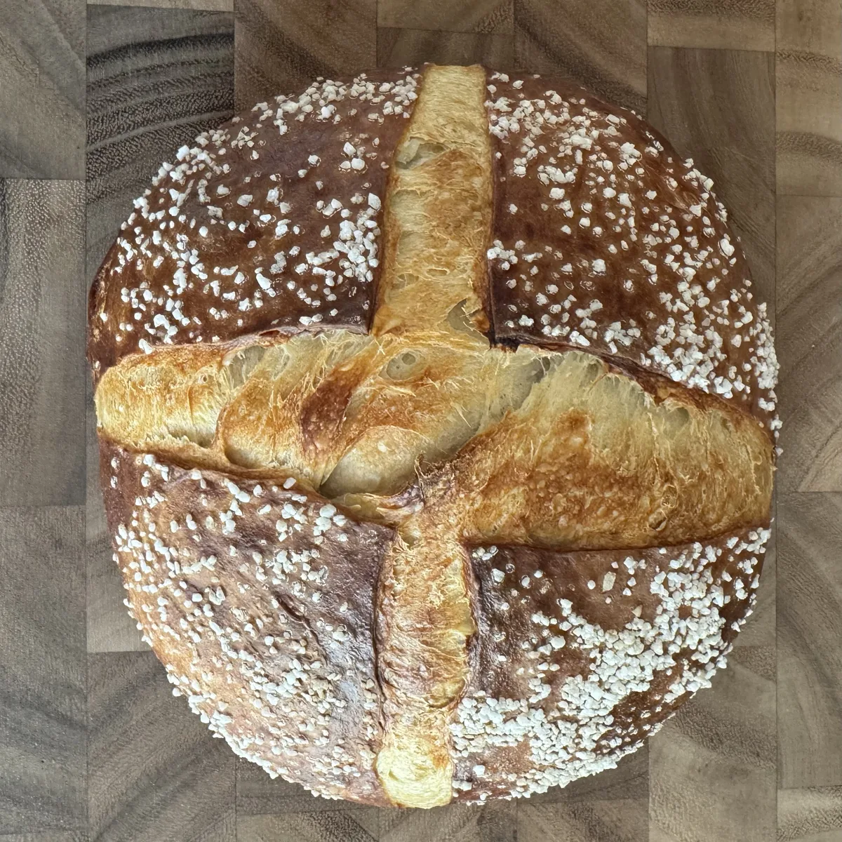 A deep brown Pretzel loaf scored in a cross with coarse salt scattered over it